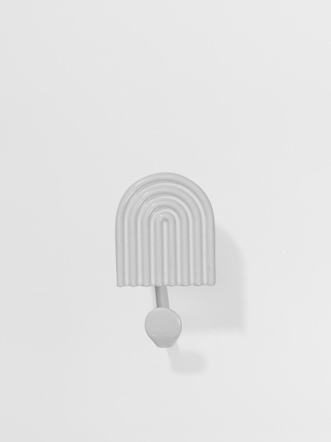 Decorative white wall hook with arch design on a light gray background